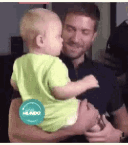 a man is holding a baby in his arms and the baby is kissing the man .