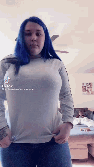 a woman with blue hair is standing in a living room wearing a white shirt .