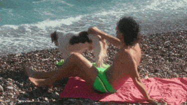 a man laying on a pink towel on the beach with a dog