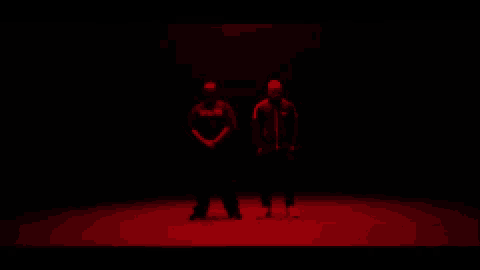 two men are standing next to each other in a dark room in red lights .