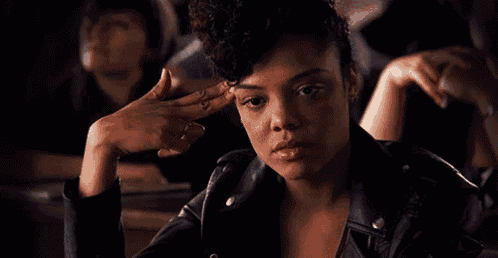 a woman in a leather jacket is sitting at a table with her hand on her head .