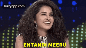 a woman with curly hair is smiling and laughing while wearing earrings and a white shirt .