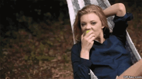 a woman is sitting in a hammock and eating an apple .