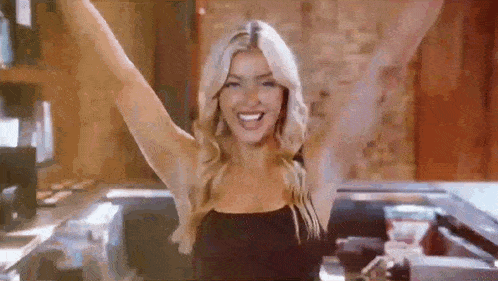a woman in a black dress is raising her arms in the air .