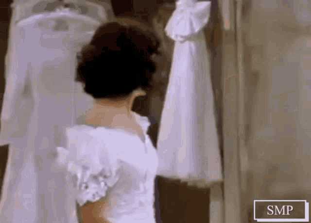a woman in a white dress is standing in front of a mirror looking at herself .