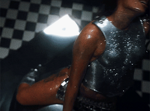 a woman in a silver tank top is sitting on a checkered floor