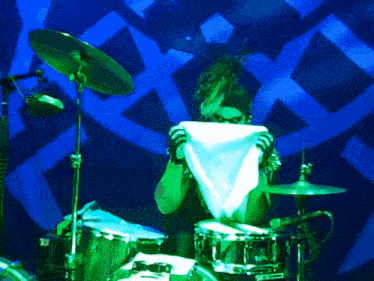 a drummer is covering his face with a white cloth in front of a blue background