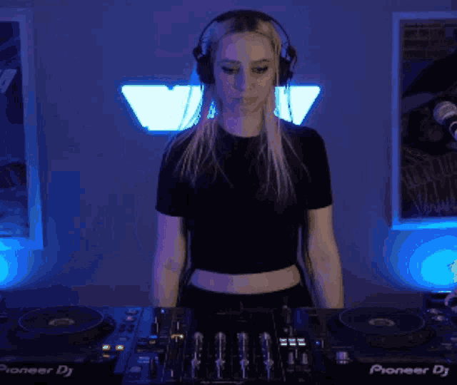 a woman wearing headphones stands in front of a pioneer dj
