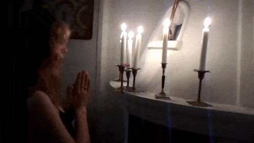 a woman is praying in front of candles on a shelf