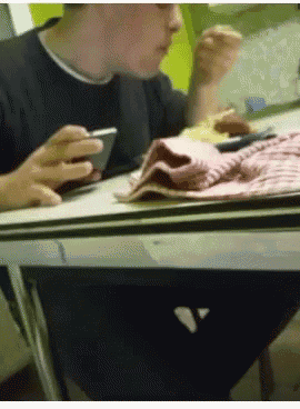 a man is sitting at a table looking at his cell phone