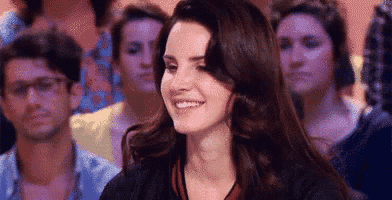 a woman is smiling in front of a crowd of people in a room .