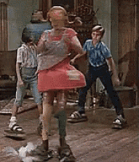 a woman in a red dress is standing on a stool in a room with two boys .