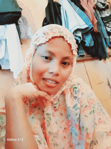 a woman wearing a floral hijab is standing in front of a galaxy a12 phone screen