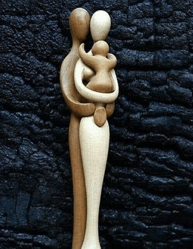 a wooden sculpture of a man and woman hugging a baby .