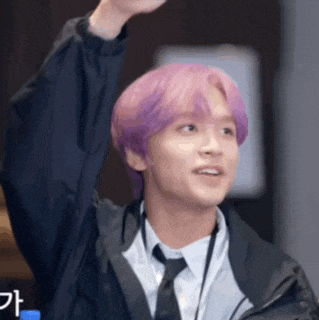 a man with purple hair is wearing a jacket and tie and raising his hand in the air .