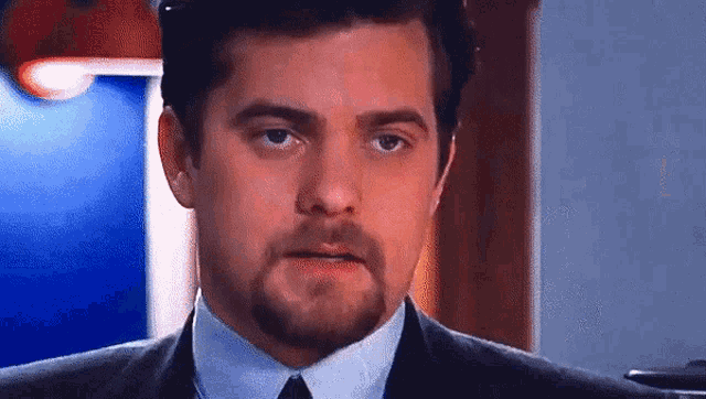 a man with a beard wearing a suit and tie looks at the camera .