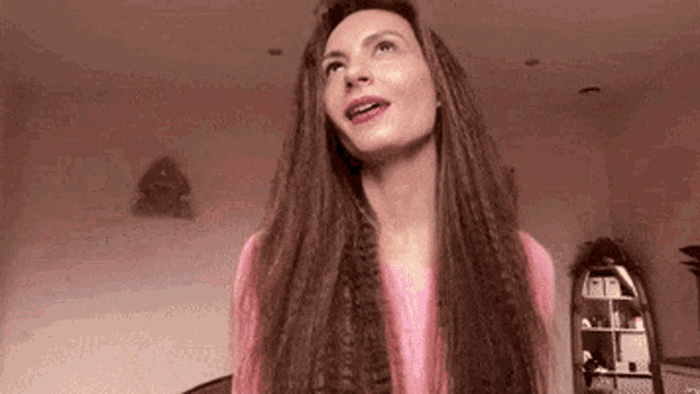 a woman with long hair and dreadlocks is wearing a pink shirt and making a funny face .