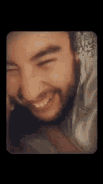 a close up of a man with a beard smiling while laying in bed .
