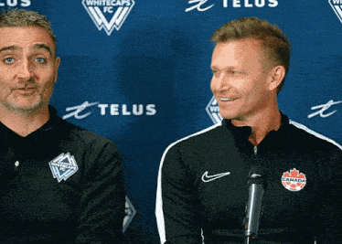 two men sitting in front of a telus wall