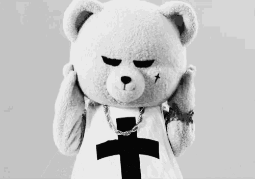 a black and white photo of a teddy bear wearing a cross shirt and chain .