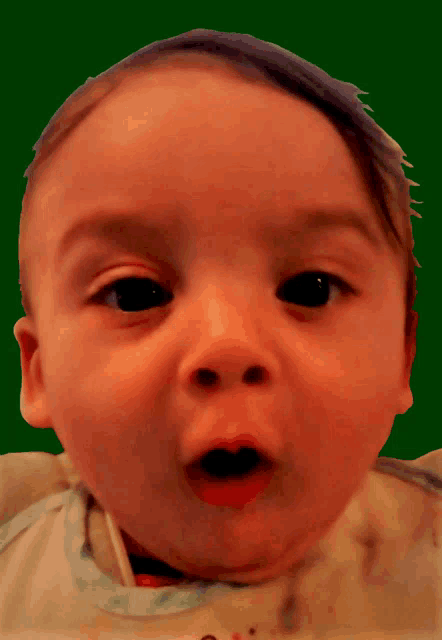 a baby with a green background making a funny face