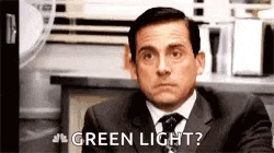 a man in a suit and tie is sitting at a desk and saying `` green light '' .