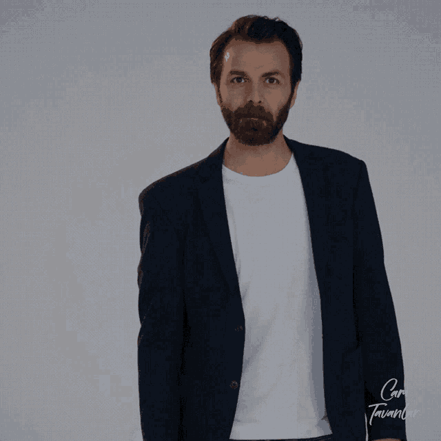 a man with a beard is wearing a black jacket and a white t-shirt that says cami tavanlar