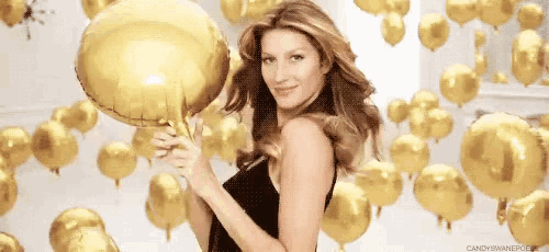 a woman in a black dress is holding a gold balloon in front of gold balloons .