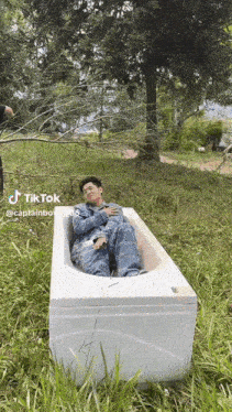 a man is laying in a bathtub in the grass with a tree in the background .