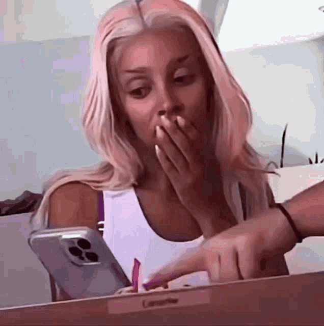 a woman with pink hair is covering her mouth while looking at a cell phone .