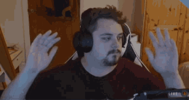 a man with a beard is wearing headphones and waving his hands while sitting in front of a computer .