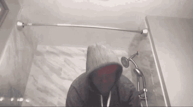 a person in a hoodie is standing in a shower with a shower head .