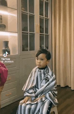 a little boy is sitting on a stool in a room wearing a striped cape .