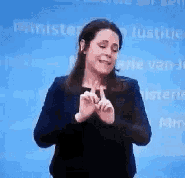 a woman is making a heart shape with her hands while standing in front of a blue background .