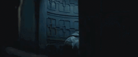 a man in a batman costume is standing in a dark room looking at another man .