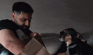 a man and a dog are sitting on a couch looking at a bag .