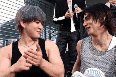 two men are sitting next to each other and one is wearing a tank top that says ' nct dream ' on it