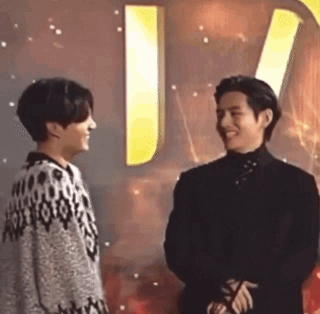 two men are standing next to each other and smiling at each other on a stage .