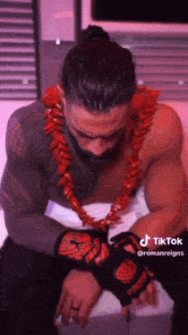 a shirtless wrestler wearing a red lei and gloves is sitting on a bed .