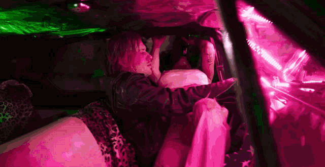 a man is sitting in a car with a pink and green light behind him