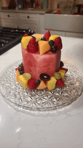 a watermelon cake with fruit on top is on a glass plate