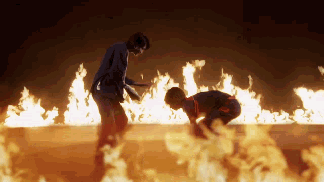 a couple of people are standing in front of a fire