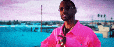 a man wearing a pink shirt and sunglasses is pointing at something .