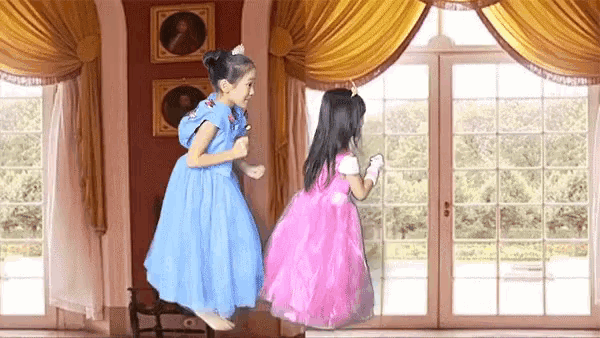 two little girls in dresses are jumping in a room .