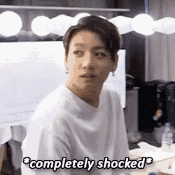 a young man in a white shirt is standing in front of a computer screen and says `` completely shocked '' .