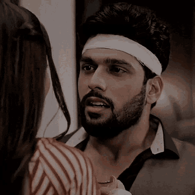 a man with a beard wearing a headband talks to a woman