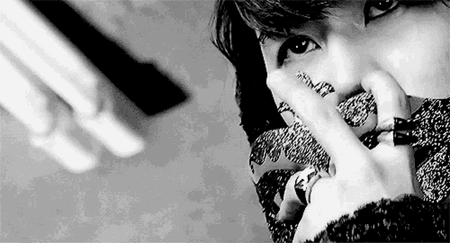 a black and white photo of a person wearing rings on their fingers covering their face .
