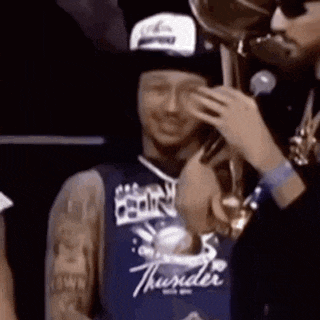 a man in a thunder jersey is talking on a cell phone while holding a trophy .