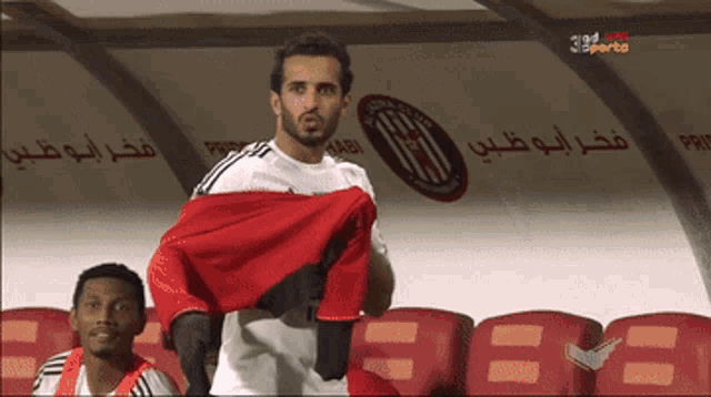 a man in a white shirt holds a red and black flag in front of a sign that says ' juba club '