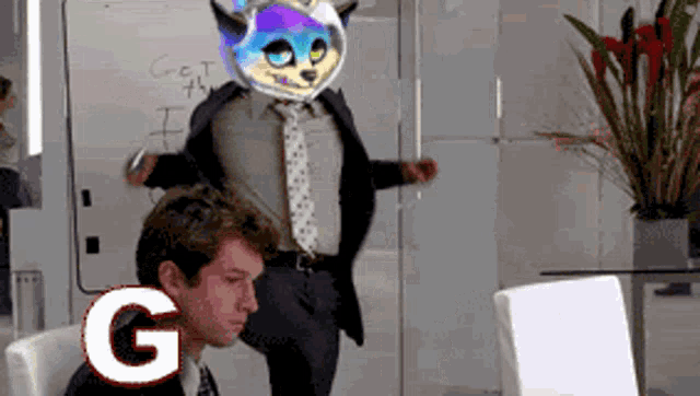 a man in a suit and tie is sitting at a desk in front of a white board that says get the i